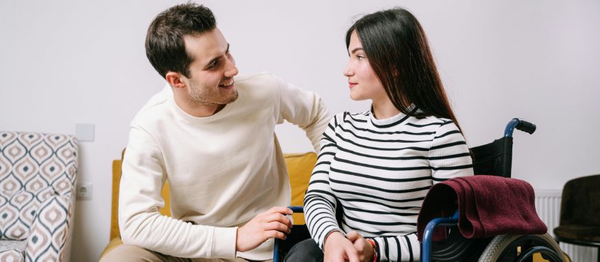 A woman in a wheelchair with a man sat on a chair