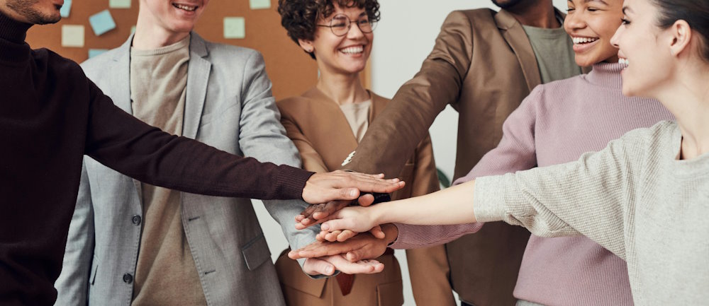 A group of people stood in a semi circle all reaching one of their hands in to the middle