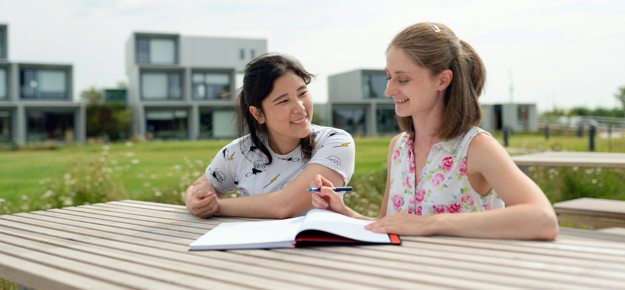 Two young women sat outside at a table with notebook