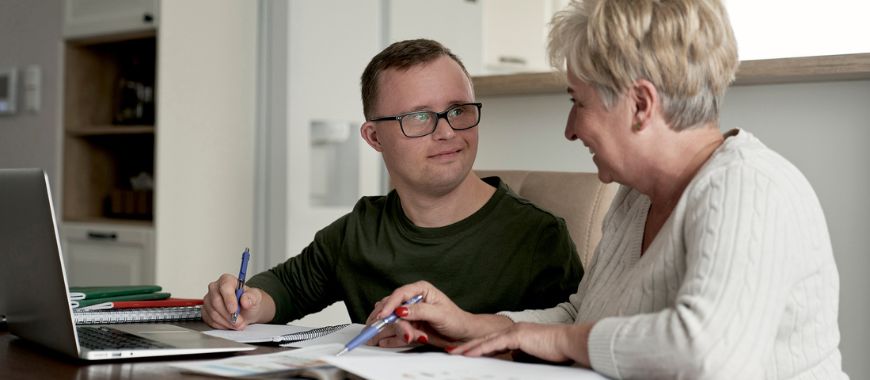 A young man with learning difficulties sat with an older woman, working at a desk
