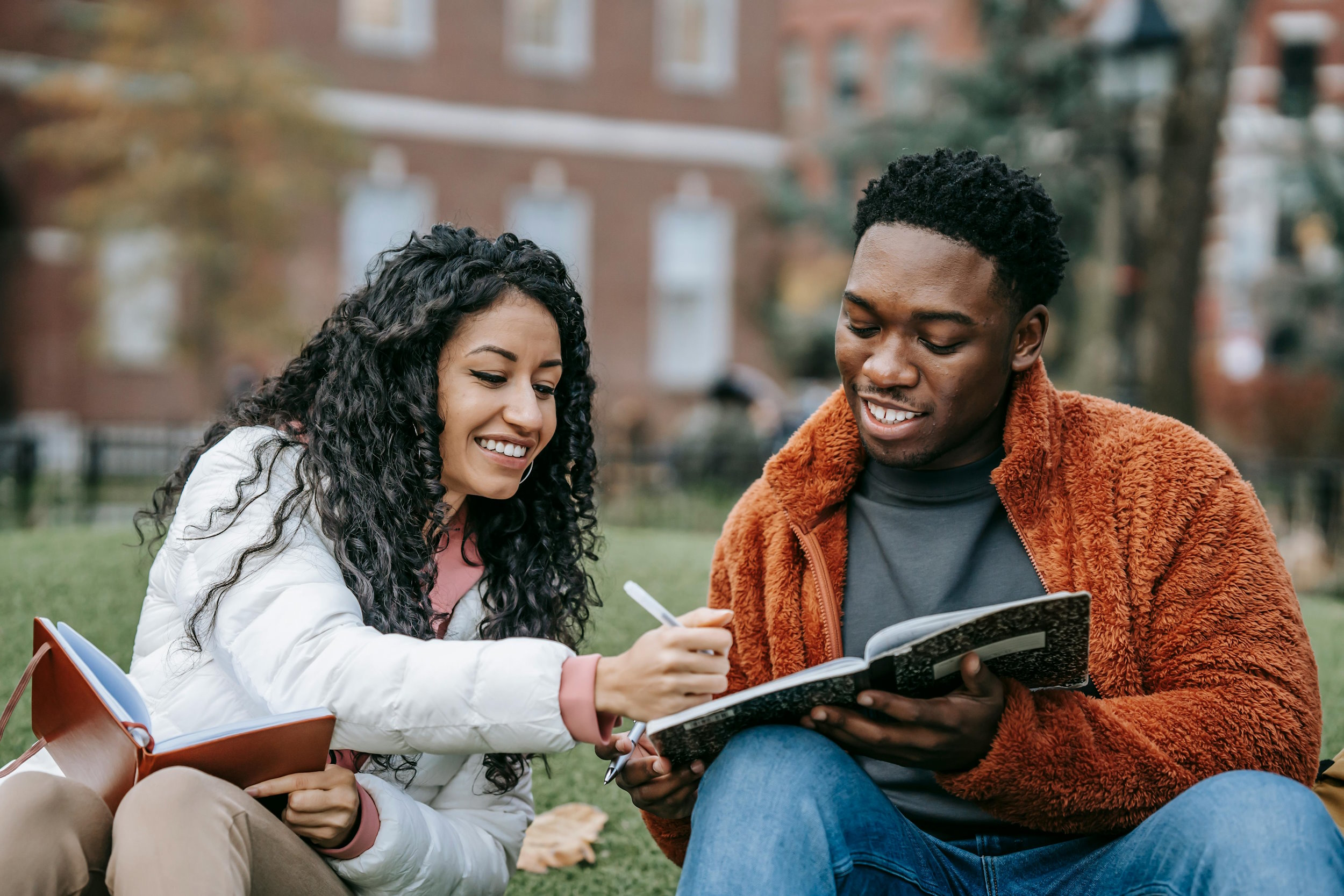 A young woman and man sat on the grass doing some college work