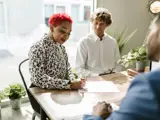 A woman sat at a desk signing a piece of paper with two men sat with her