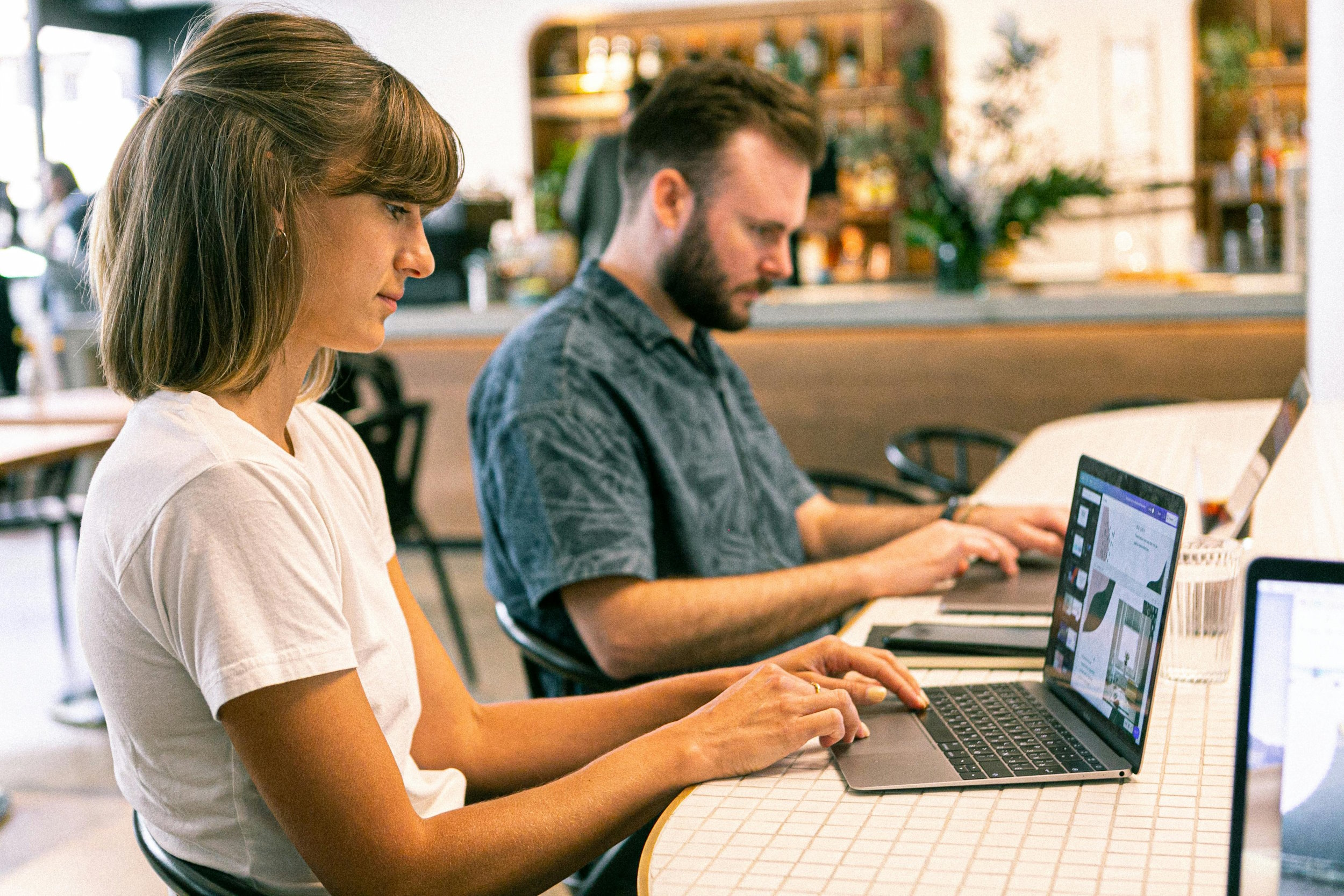 A young woman and man sat at a desk working on laptops